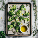 Roasted broccoli on a baking sheet with herbs and olive oil.